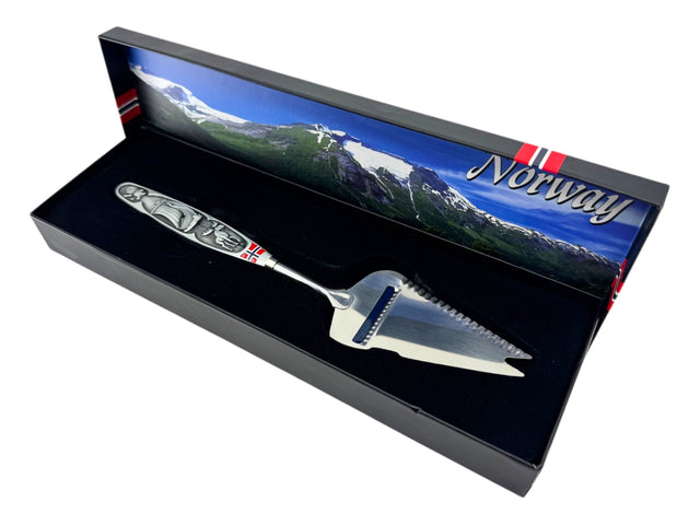 A jagged Norwegian cheese slicer & cutter with a pewter handle featuring a Viking ship and moose image, presented in a box—a tribute to Scandinavian heritage.