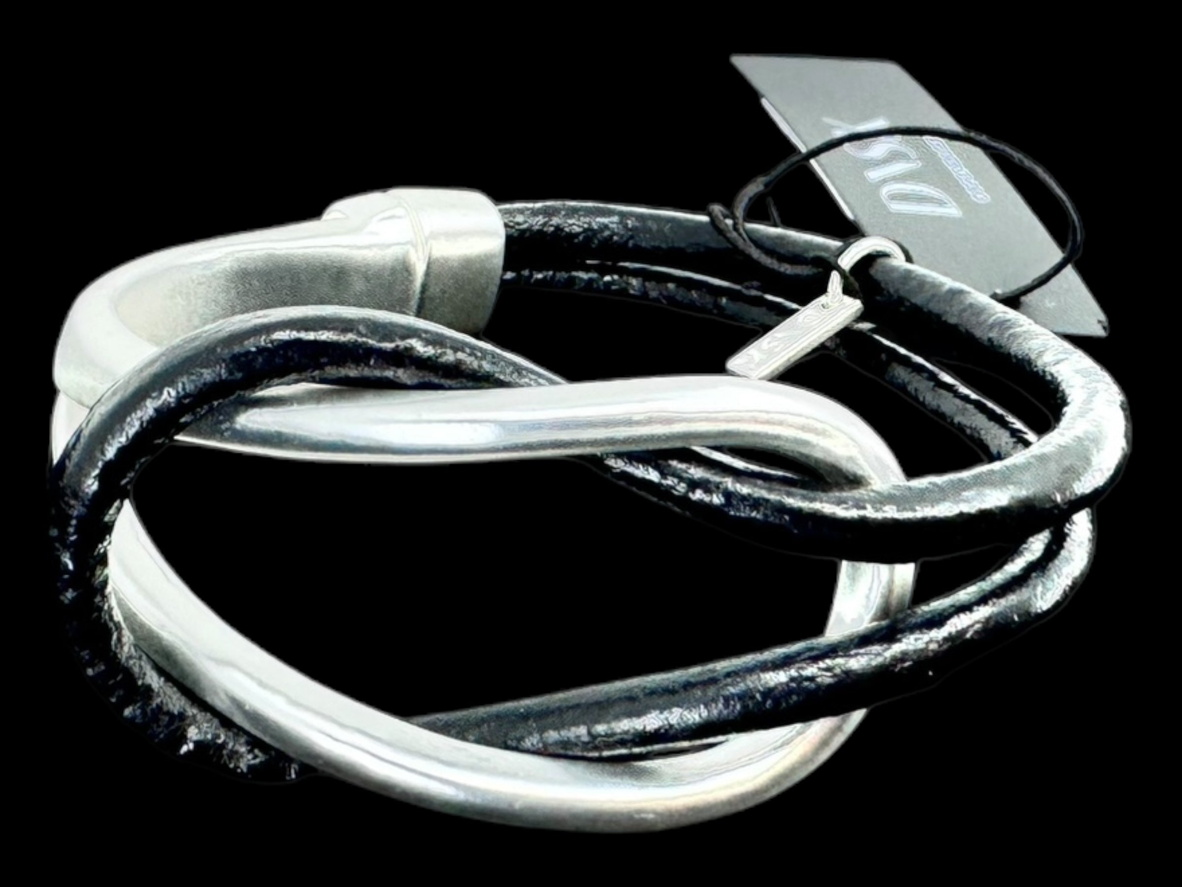 The "Bracelet: Nostalgia Togetherness Leather" presents a minimalist Nordic design with black and silver twisted elements, complemented by a magnetic clasp and an attached tag. Its blend of intertwined metal and leather exudes an elegant, understated style suitable for any occasion.