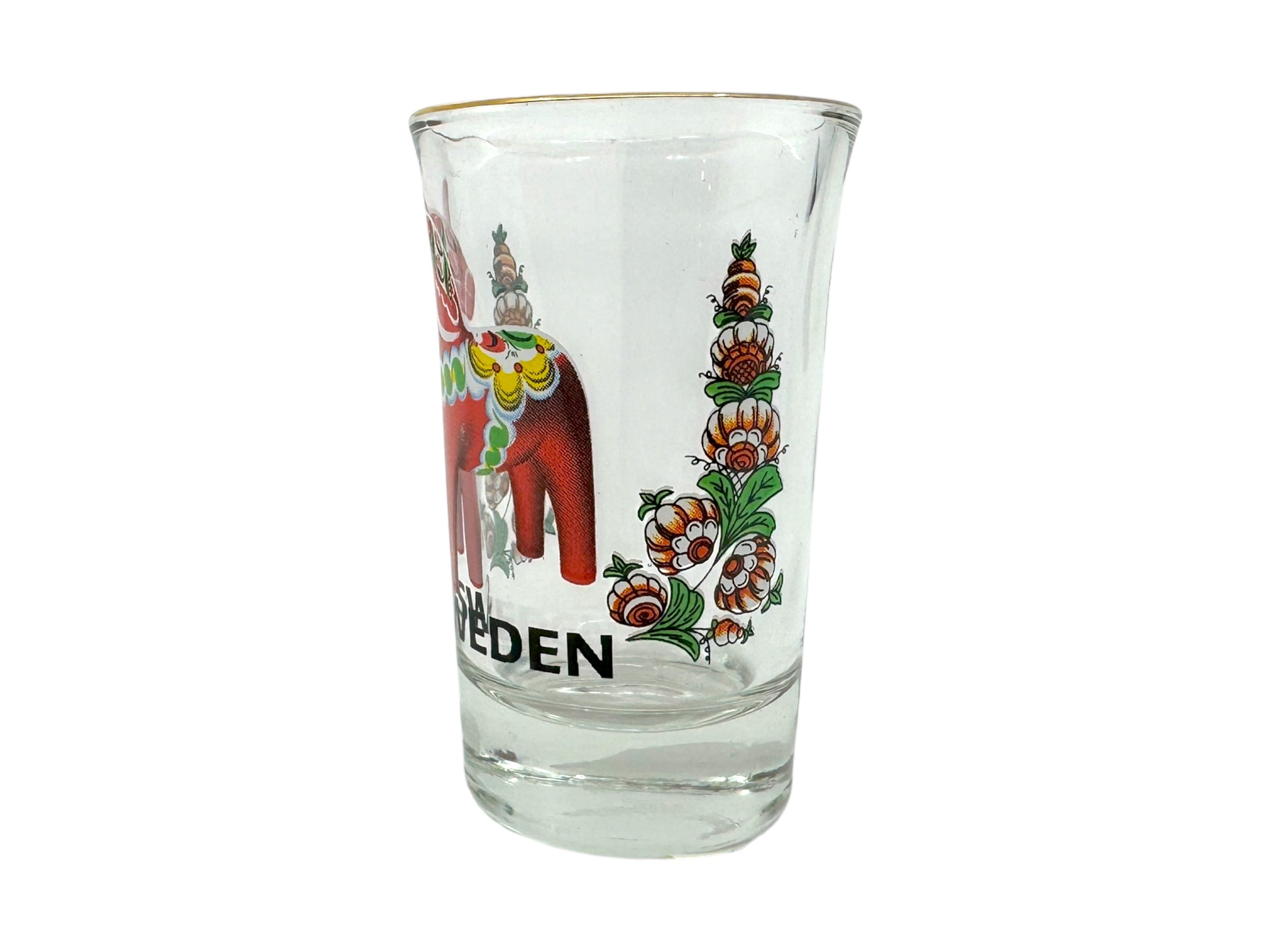 The Shot Glass: Sweden Red Dala Horse features a clear glass with a red Dala horse and green, red, and orange floral designs. “SWEDEN” is printed at the bottom—an ideal Nordic souvenir inspired by Scandinavian folk art.
