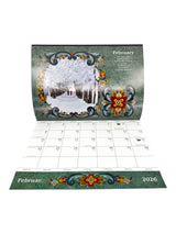 The Calendar: Norway 2026 Wall Calendar – Visions & Verse of Vikingland displays February 2026 with floral motifs and a winter scene inspired by Norwegian culture, featuring people strolling in a snowy park.