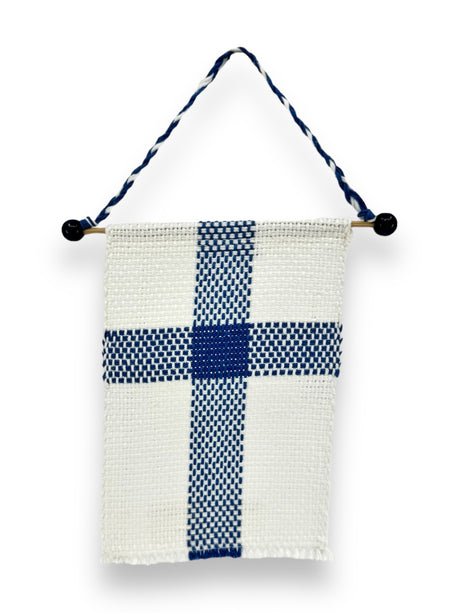 The Flag: Small Finnish Flag on Hanger (6.5"x4") is a hand-woven wall hanging made from 100% cotton, showcasing a blue cross on a white background reminiscent of the Finnish flag. It is stylishly hung by a twisted cord connected to a wooden dowel decorated with black beads.