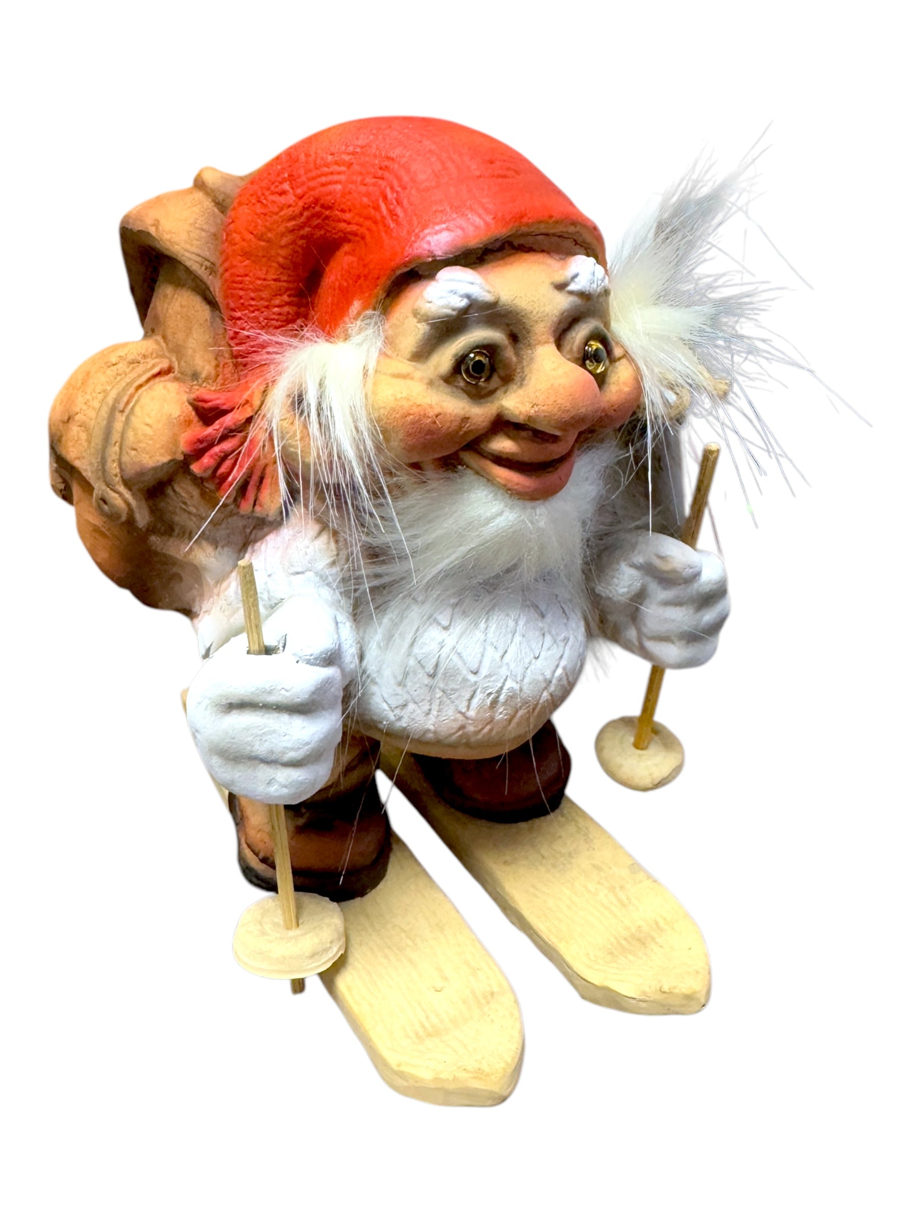 The Troll: NyForm - Nissen on Skis with Backpack is a delightful gnome figurine featuring a red hat and white beard, skillfully skiing with poles while carrying a backpack. This charming piece of Norwegian design makes an excellent addition for collectors.