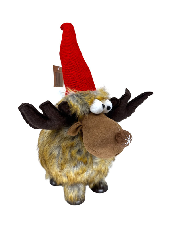 The Decor: Shaky Moose Holiday Table Decoration is a 16 plush moose with brown antlers, yellow-brown fur, and a red poseable hat—ideal for Christmas centerpieces or Scandinavian-inspired décor. Shown on a white background.