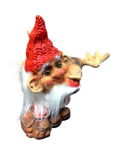 Introducing the delightful "Troll: NyForm - Troll Feeding Moose" figurine, showcasing a gnome with a red hat, white beard, and cheerful expression. The gnome is depicted holding a moose head against a light background, making it an ideal collectible for those who appreciate unique designs inspired by Norwegian style.