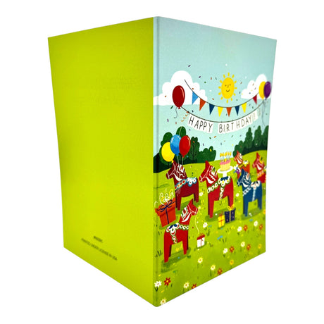 The Dala Horse Party Birthday Card is a vibrant Swedish card that stands upright, showcasing Dala horses, presents, balloons, and a Happy Birthday banner in charming folk art style on a cheerful green outdoor scene.