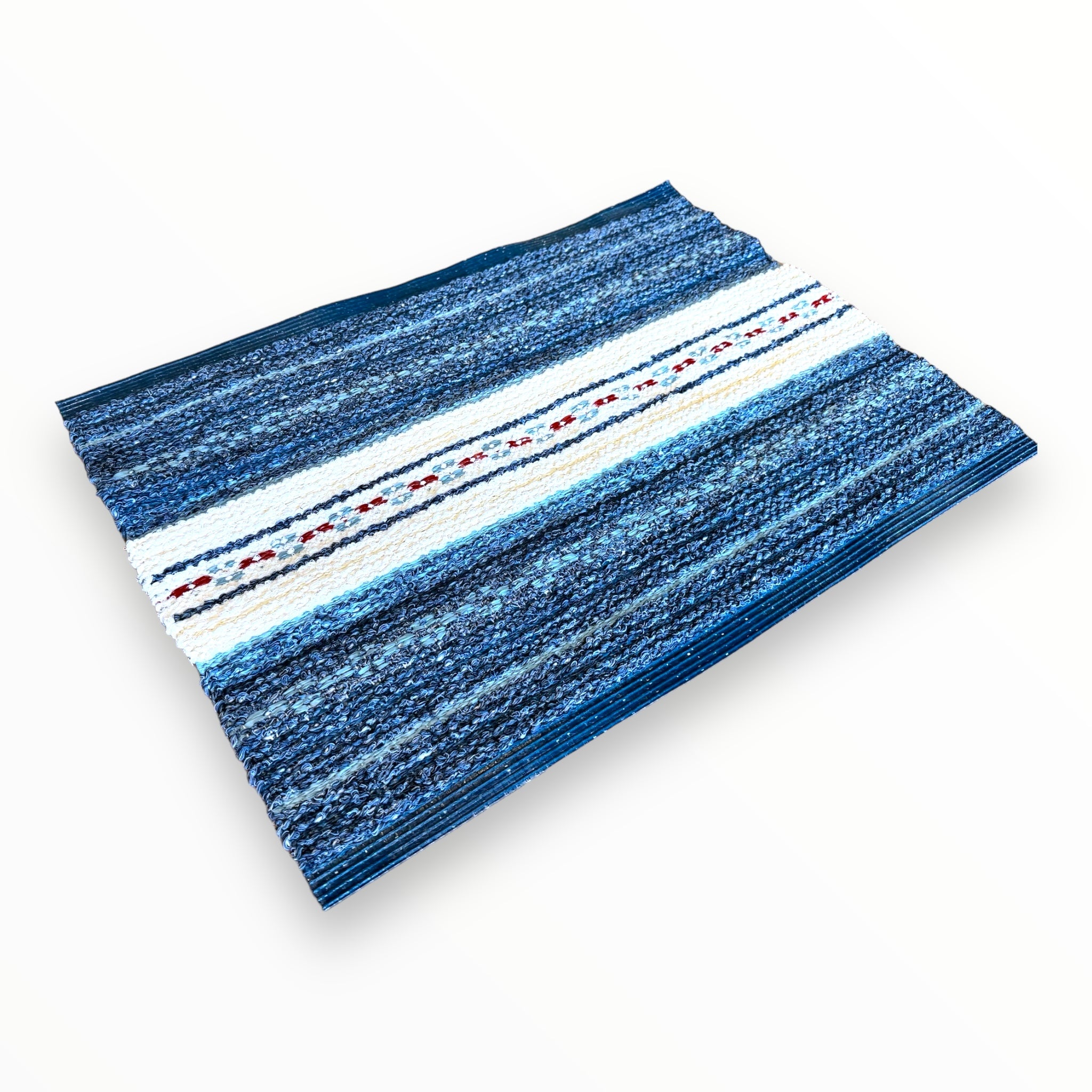 The Rug: Mixed Asta - Blue, crafted from cotton and vinyl in Sweden, is perfect for both indoor and outdoor use. It features a durable design with blue horizontal stripes and a central white stripe embellished with red and blue geometric patterns.