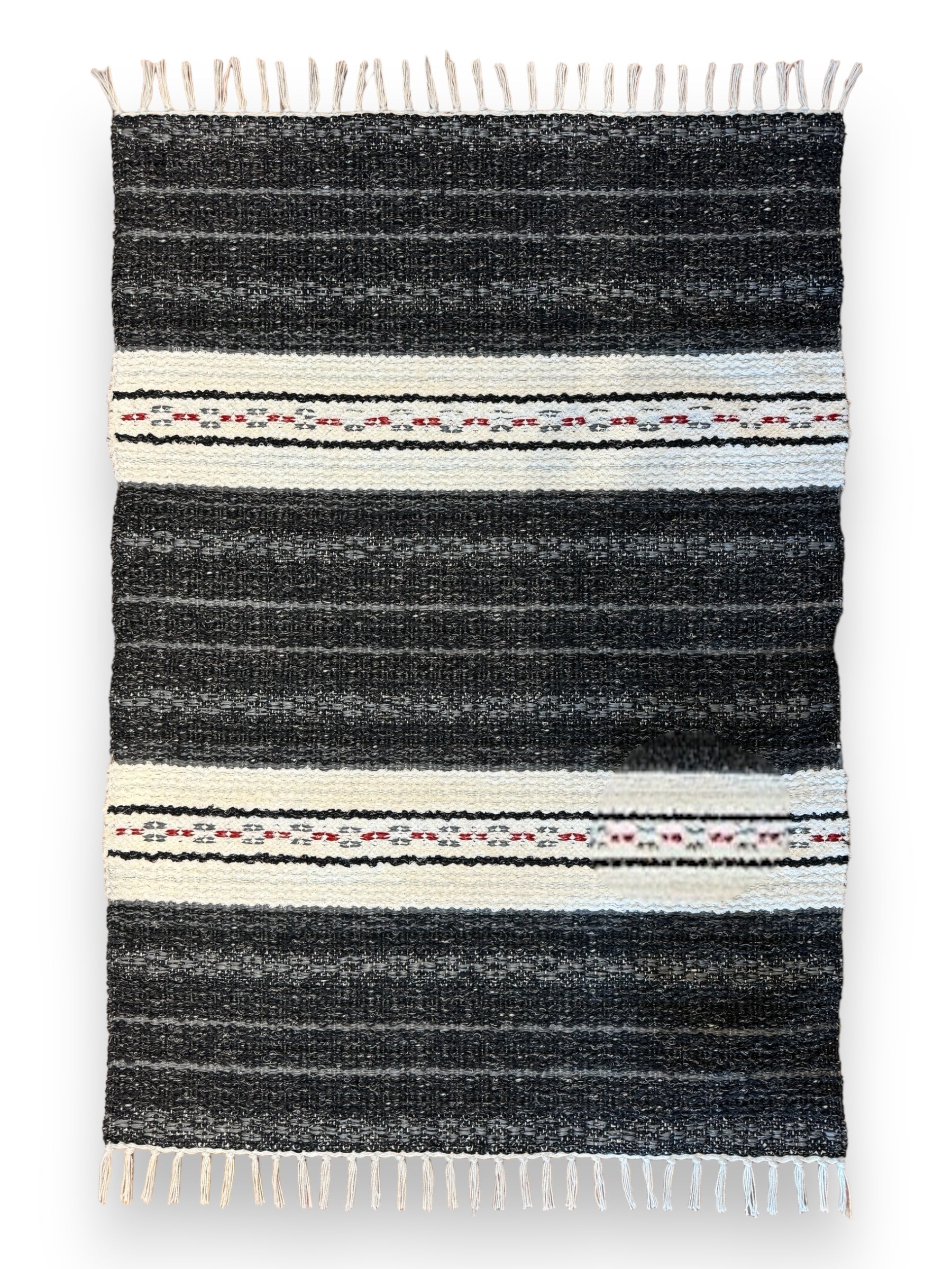 Introducing the Rug: Mixed Asta - Black, crafted from cotton and Swedish vinyl. This durable rug, designed for both indoor and outdoor use, features a woven black base with two white horizontal stripes, accented by small patterns in red, green, and black. The fringed edges add a stylish flair to any space.