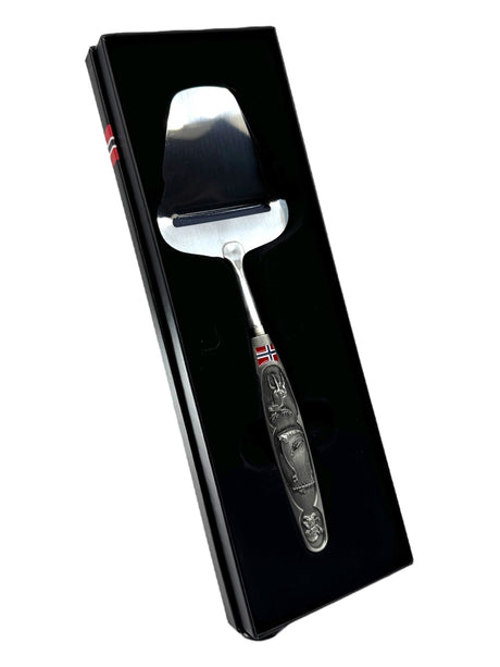 A Norwegian cheese slicer with a pewter handle featuring images of a Viking ship and moose, presented in a black gift box—perfect for celebrating Nordic heritage.