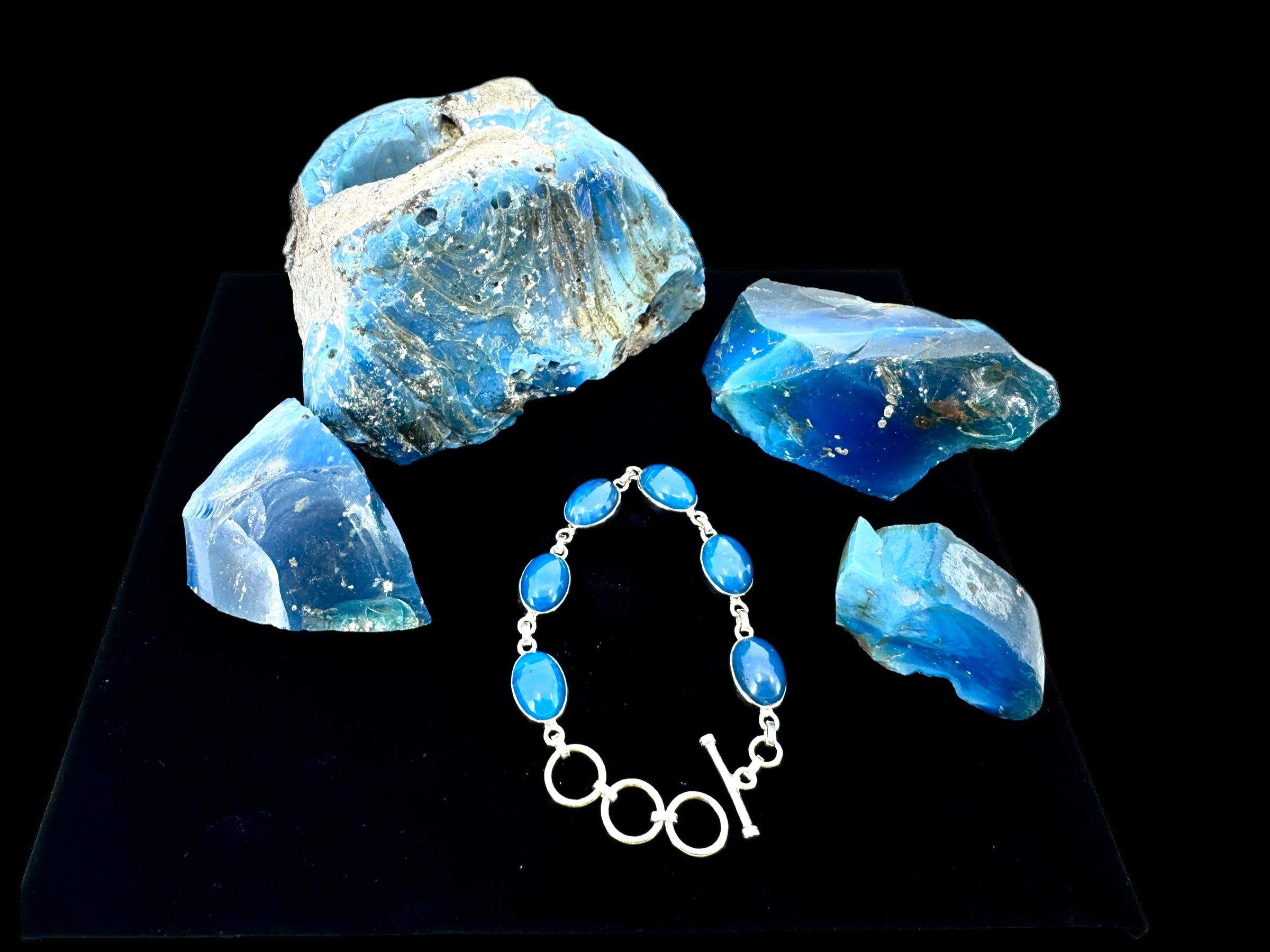 The "Plain Oval Seven Stone" silver bracelet with blue gemstones is displayed on a black surface.