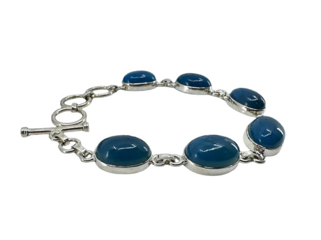The Plain Oval Seven Stone Swedish Blue Sterling Silver Bracelet features Swedish Blue oval stones linked in series with a toggle clasp on a black background.