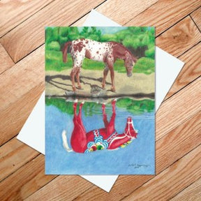 A vibrant image of a spotted horse, akin to a Dala Horse, stands by a pond with its colorful, abstract reflection reminiscent of Scandinavian design, similar to the artwork featured on the "Dala Horse Reflection" 5x7 card.
