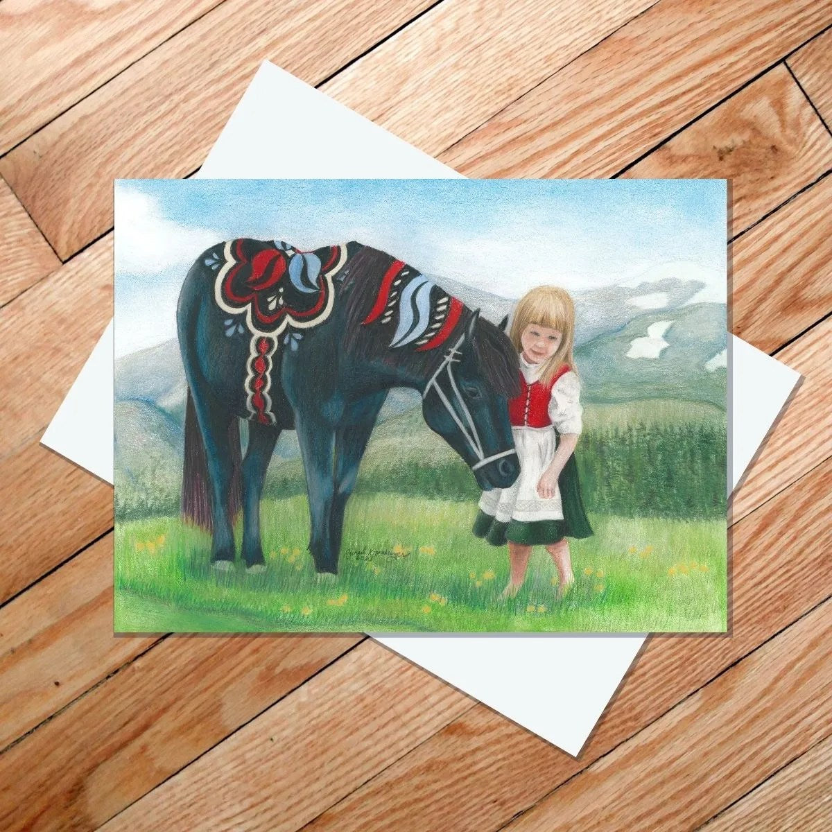 A color pencil drawing on the "Don't Be Shy" 5x7 card features a young girl in a dress standing next to a dark horse adorned with a decorative saddle, reminiscent of Dala ponies, against the backdrop of a grassy field and mountains.