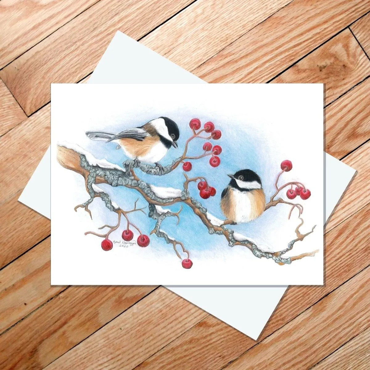 This 5×7-inch blank card, titled "Black Capped Chickadees," features an illustration of two birds atop a snow-draped branch with red berries. Seamlessly capturing nature's essence, it embodies the unique style of Rachael Koppendrayer, making it perfect for any occasion or heartfelt message.