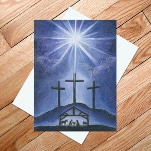 The "Star of the East" 5x7 card, featuring a nativity scene with three crosses on a hill, two doves, and the Bethlehem star shining above, is placed on a wooden surface.