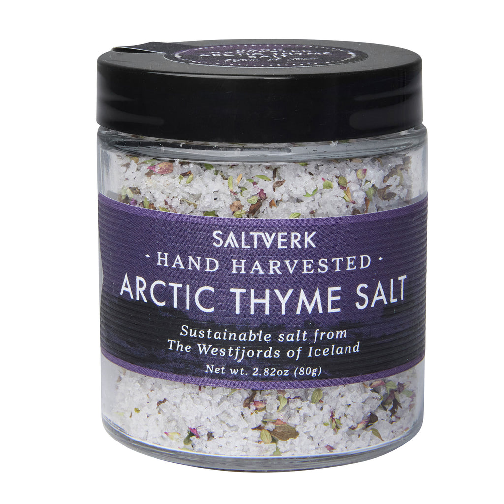 A jar of Saltverk Arctic Thyme Salt, featuring a black lid and purple label, highlights the hand-harvested salt from Iceland's picturesque countryside. Perfect for curing meat, this blend weighs 80g (2.82 oz).