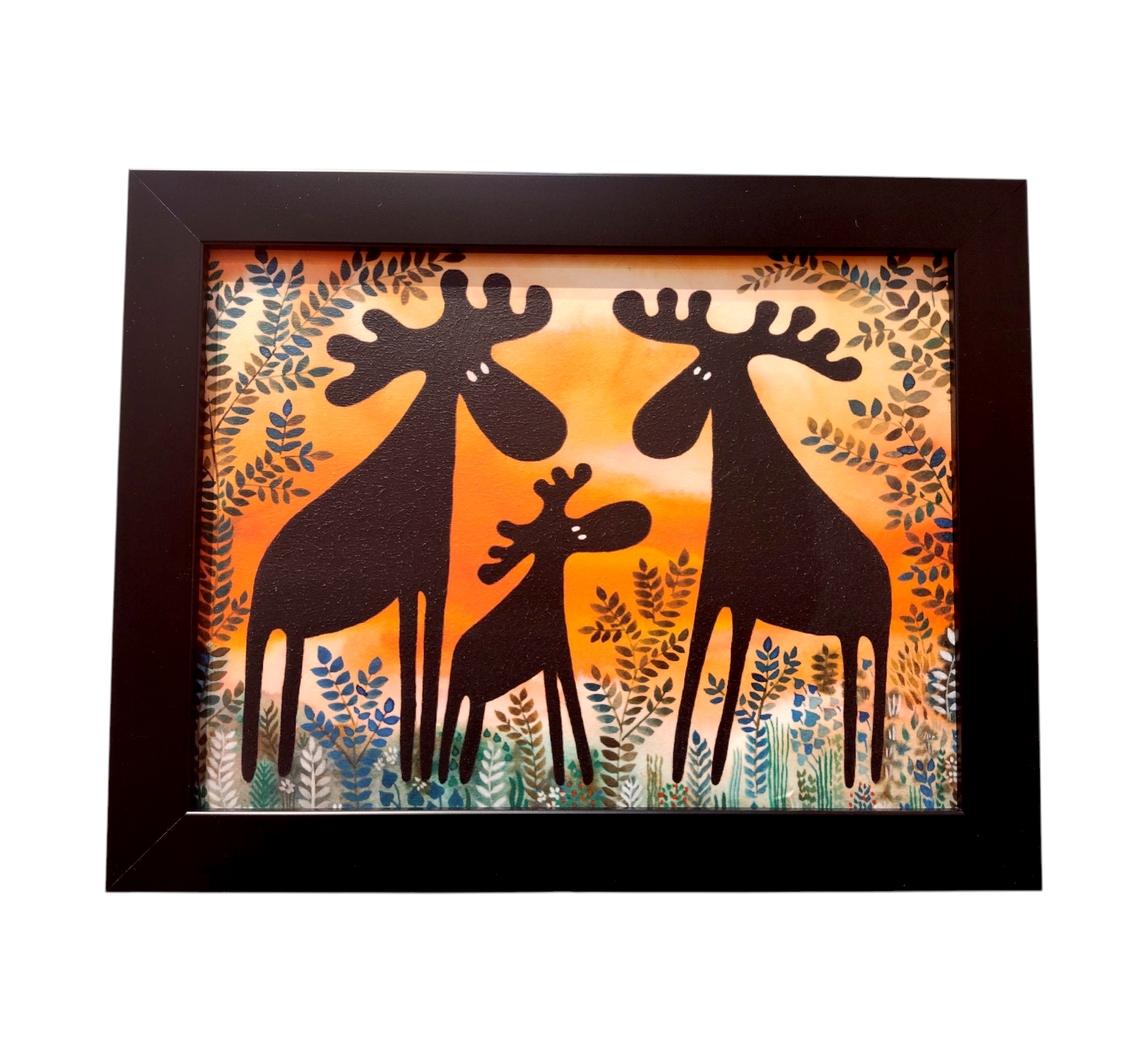 The Three Moose Evening Sunset acrylic art showcases two adult moose and a calf silhouetted against a vibrant orange and green leafy sunset, framed for a Scandinavian aesthetic.