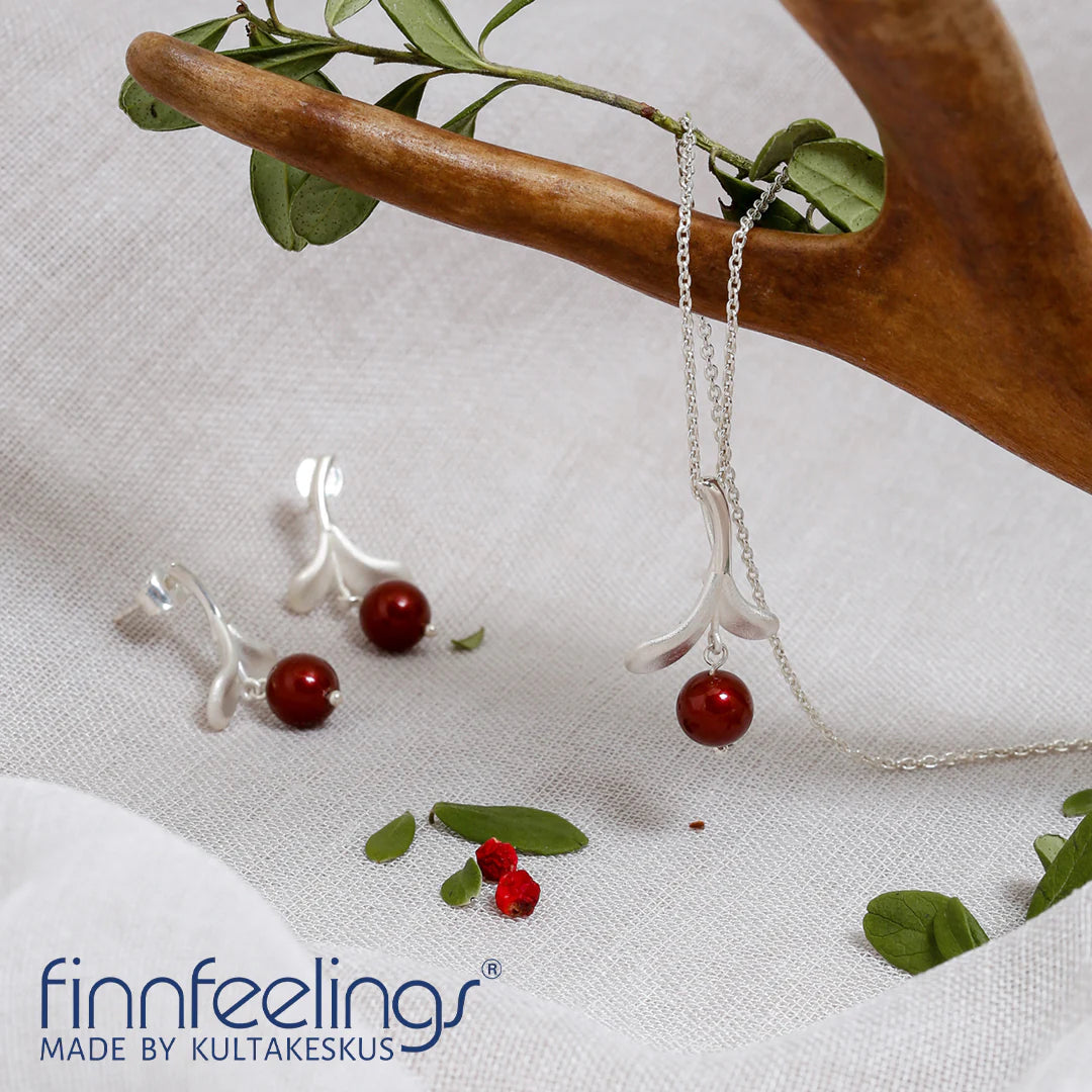 A Lingonberry Silver Necklace with matching earrings adorned with red stone accents is displayed on a light fabric, featuring Scandinavian-inspired branch and leaf designs reminiscent of traditional Finnish jewelry artistry.