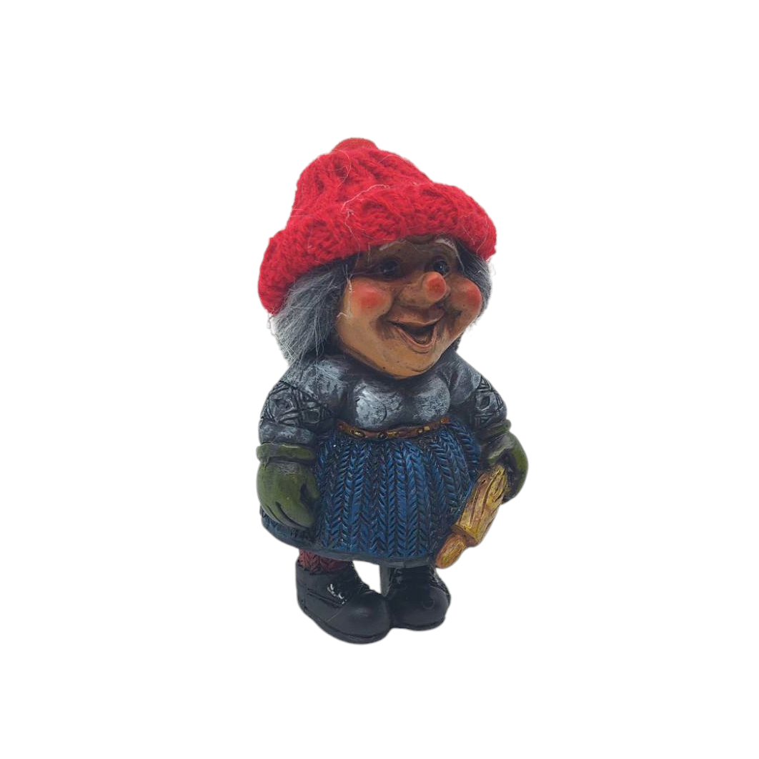 A charming Scandinavian figurine, often mistaken for a Nisse wife, features a red knit hat, blue skirt, and green gloves while holding a gold-colored rolling pin.