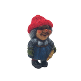 A charming Scandinavian figurine, often mistaken for a Nisse wife, features a red knit hat, blue skirt, and green gloves while holding a gold-colored rolling pin.