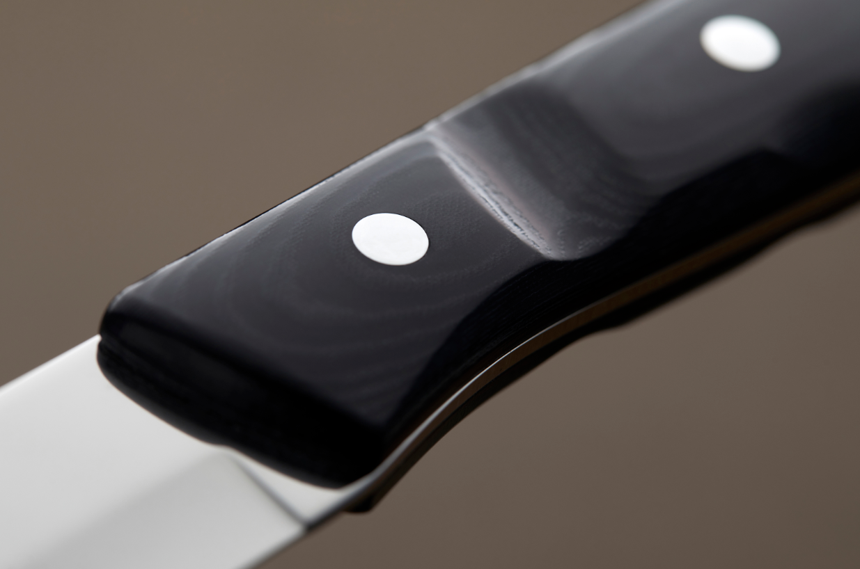 Close-up of the Gense: Old Farmer Micarta Steak Knife - Steel, featuring a sleek black grip with shiny metal rivets and part of its stainless steel blade.