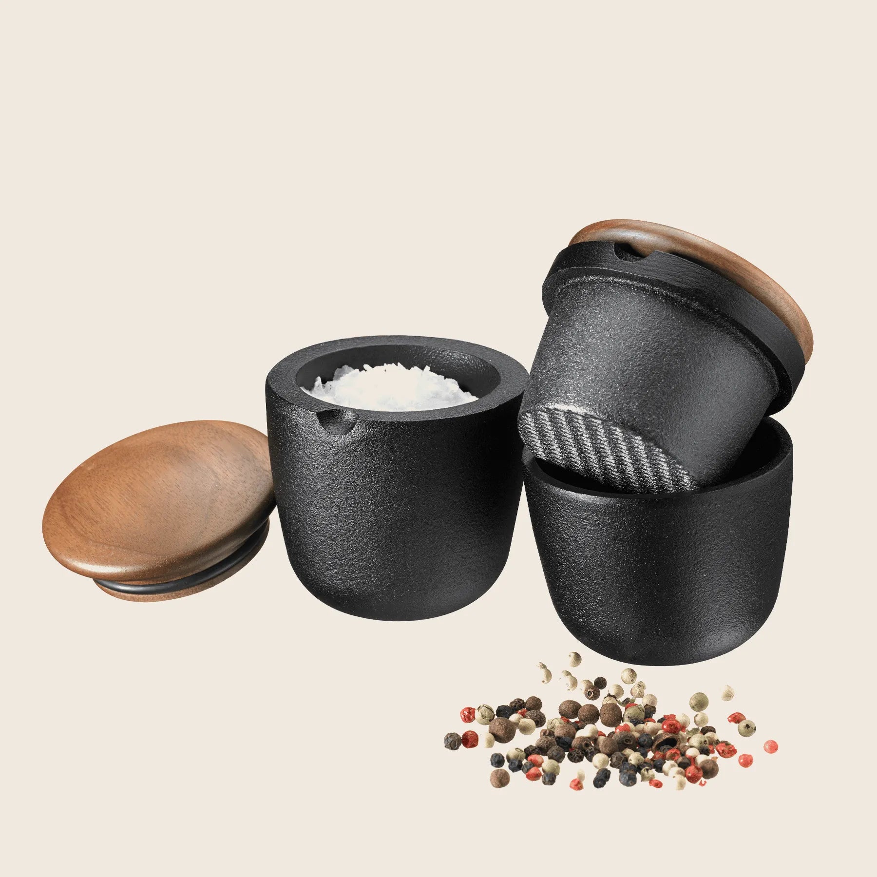 Three black containers feature walnut lids; one holds salt, another is the Skeppshult Swing Spice Mill with a built-in grinder, and scattered peppercorns nearby.