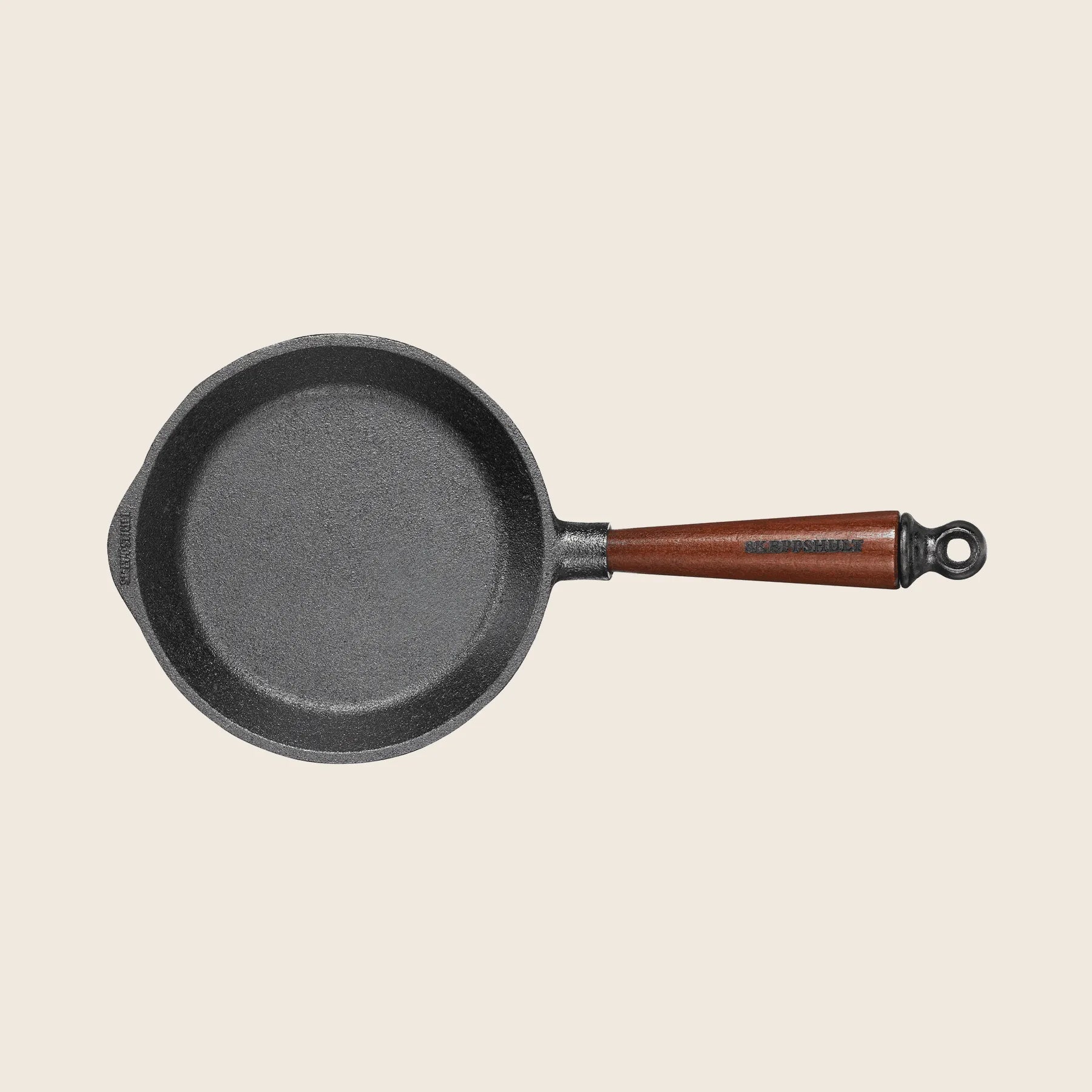 The Skeppshult Skillet with Walnut Handle 7/18cm, in black cast iron, rests against a plain background, showcasing excellent heat conduction and a pre-seasoned surface for superior cooking.