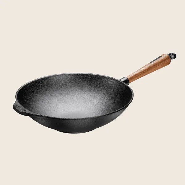 The Skeppshult Wok With Walnut Handle, 12.2 cast iron design, handcrafted in Sweden, features a natural non-stick surface and a walnut handle, standing out against a plain background.