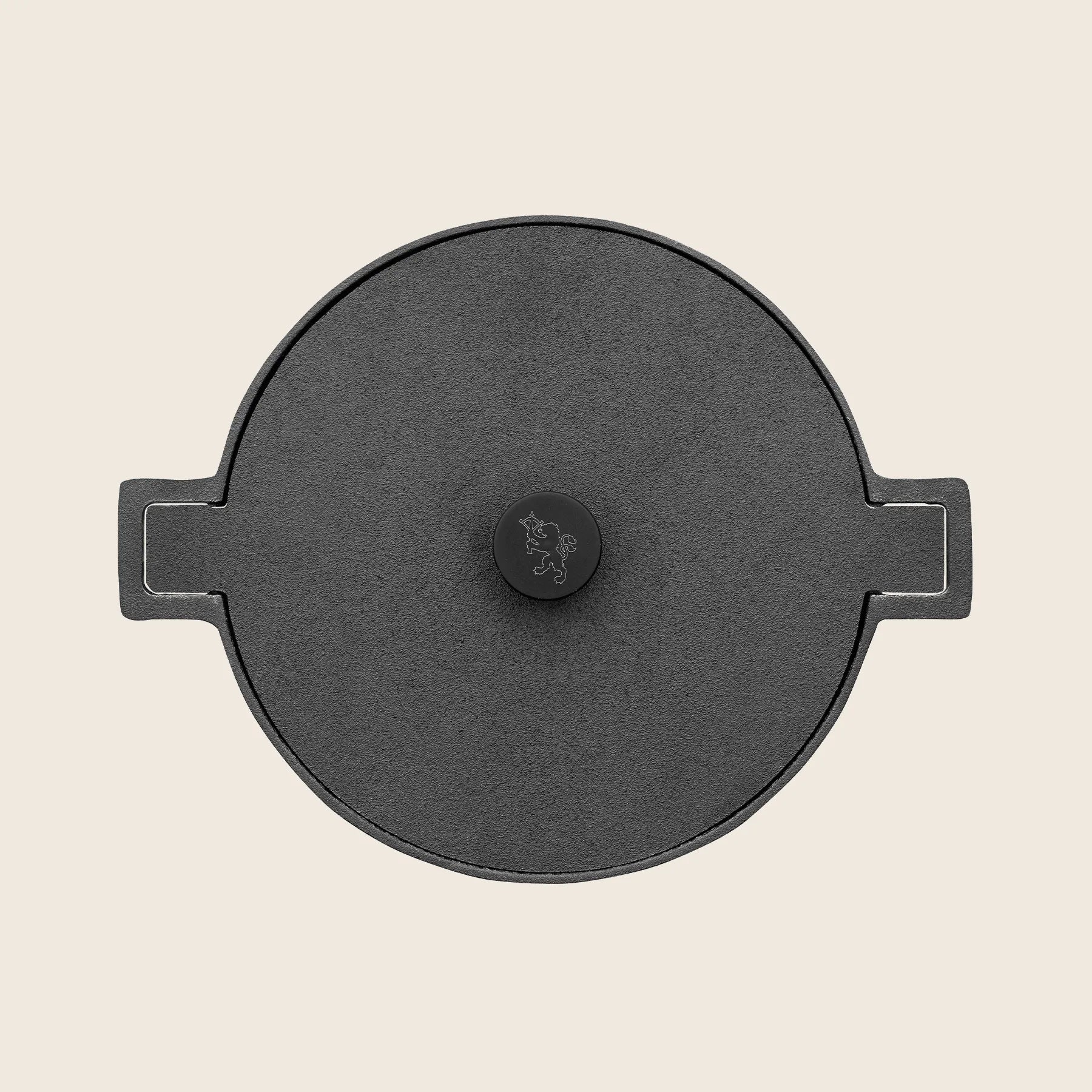 A view from above shows the black, round cast iron lid of the Skeppshult 5.25 qt Dutch Oven, seasoned with organic canola oil, featuring a central knob and two side handles on a cream background.