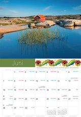 A red house on rocky shores beside calm water and reeds under a blue sky is featured for June in the Splendor of Sweden Calendar 2026.