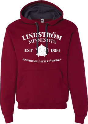 This Hoodie: Lindstrom Minnesota EST 1894 America's Little Sweden, celebrates the town known as America's Little Sweden since 1894. Made from a warm and comfortable 60/40 cotton polyester blend, it displays "Lindström Minnesota, Est 1894" in white text alongside a charming house image at the center.