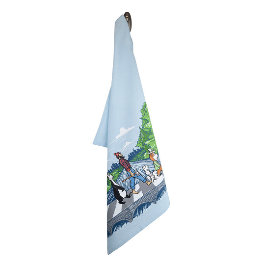 The Tea Towel: MN Abbey Road is a light blue printed cotton towel featuring an illustration by Adam Turman of three anthropomorphic skunks walking on a road with trees in the background. It's designed to hang on a hook and is machine washable for easy care.