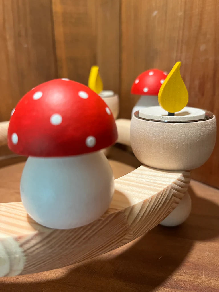 This Swedish handcrafted figurine displays a red and white toadstool with a yellow flame, stylishly placed on a curved base against a wooden backdrop.