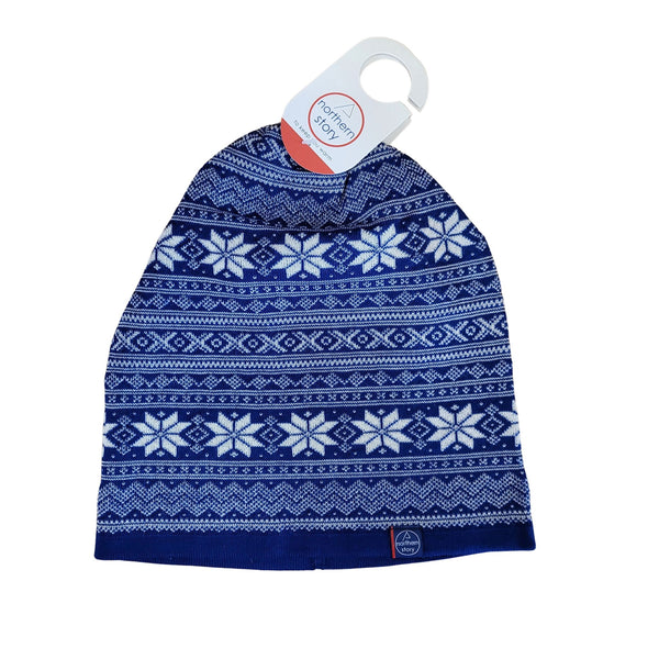 The Northern Story Setesdal Hat is a royal blue and white 100% merino wool beanie featuring a Norwegian star and geometric pattern, shown with a retail tag attached at the top.