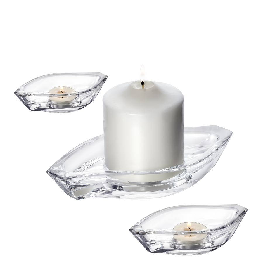 A white pillar candle burns in a glass holder, accompanied by two unlit tealights, echoing the elegance of Orrefors: Wave Votive Candle Holder 3 Piece Set. This arrangement sits on a pristine white background.