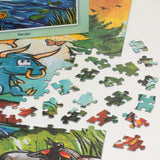 Scattered colorful jigsaw puzzle pieces reveal partial illustrations of a blue creature, butterfly, water, and greenery in cartoon style.