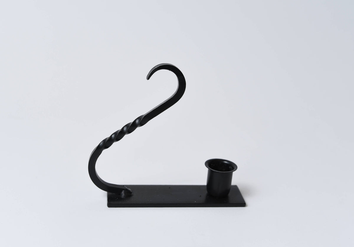 Black iron taper holder with a twisted handle, cylindrical candle cup, and rectangular base.
