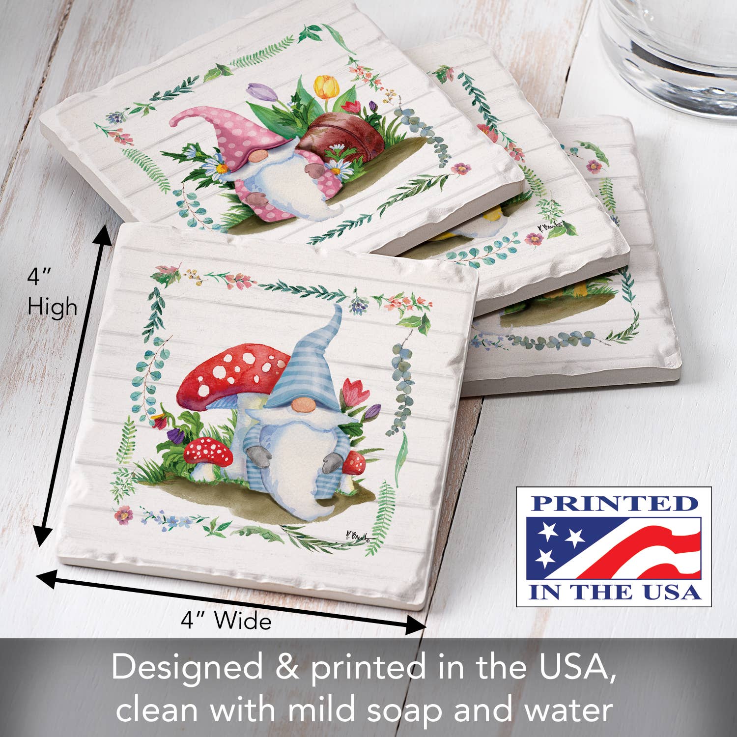 The Spring Gnomes Tumbled Tile Coaster 4-pack features charming gnome illustrations with mushrooms and flowers on absorbent stone. Each coaster includes design details, cleaning instructions, and a Printed in the USA label on the cork back.