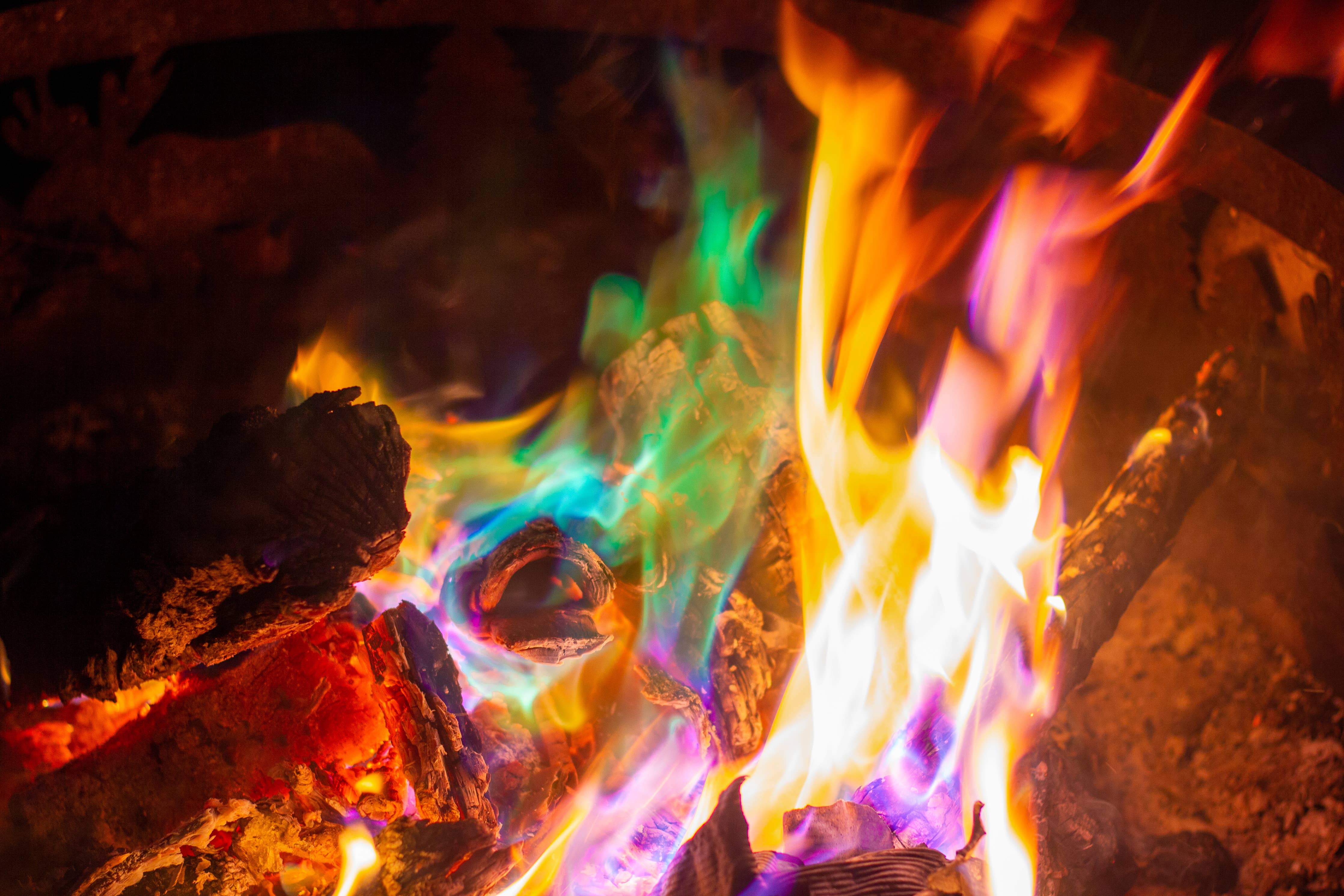 Experience a vibrant campfire with the Northern Lights - Fire Color Cones (Small Refill Pack), featuring rainbow-colored flames in shades of green, blue, purple, and yellow dancing over the logs and embers.