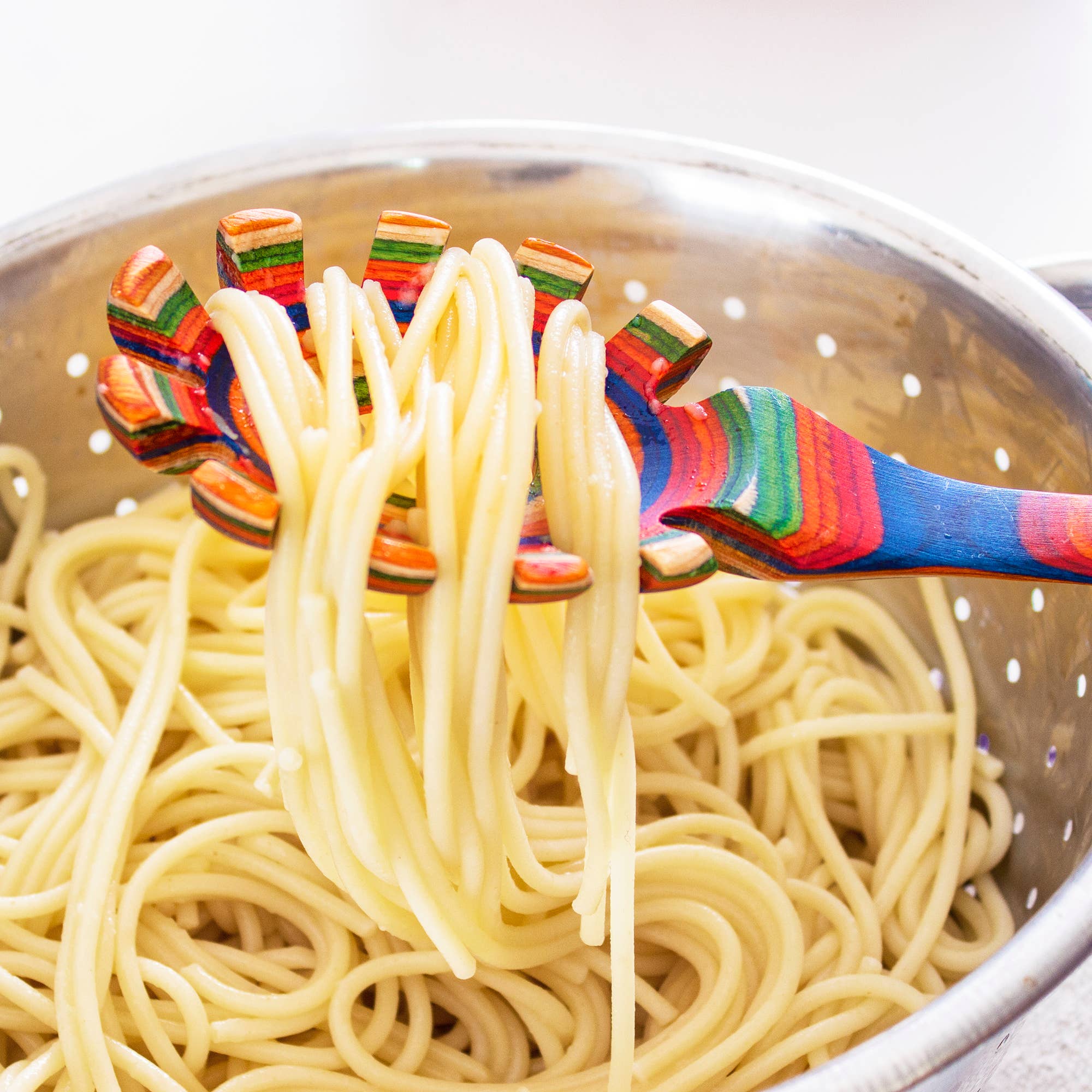 A vibrant Utensil: Marrakesh Collection Spaghetti Server gracefully lifts cooked spaghetti over a stainless steel colander brimming with more pasta.