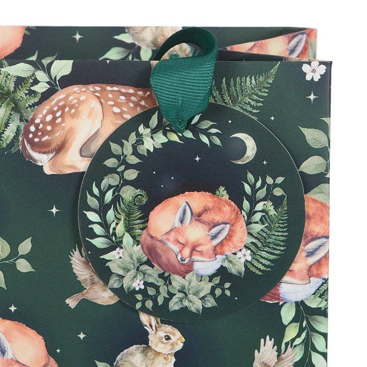 The Gift Bag: Fawn and Friends Forest Animal Print Medium Gift Bag features illustrated forest animals like a fox, rabbit, deer, and birds. It includes a round tag with a sleeping fox and foliage on a green ribbon.
