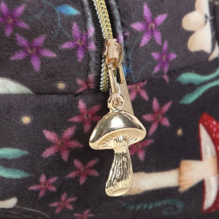 A close-up of a gold-colored mushroom-shaped zipper pull attached to a zipper on the Makeup Bag: Dark Forest Print Makeup Bag, featuring a floral and mushroom pattern in the background.