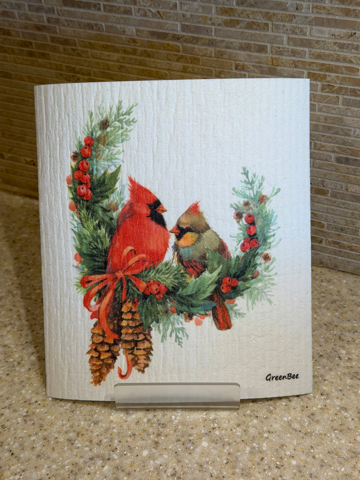 Swedish dishcloth featuring two birds perched on a wreath of pine branches, red berries, and pinecones.