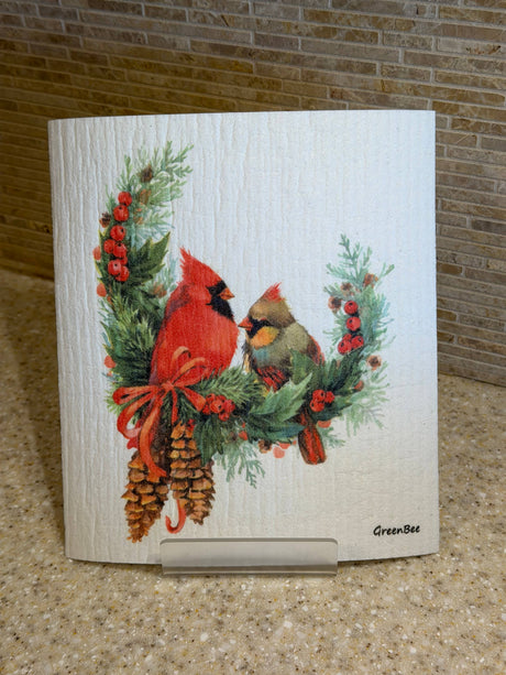 Swedish dishcloth featuring two birds perched on a wreath of pine branches, red berries, and pinecones.