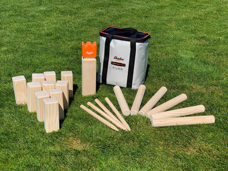 The Game: Kubb Champions Series Yard Game Viking Chess Game, featuring wooden blocks, batons, a king piece, and a carrying bag, is set up on grass—ideal for backyard fun with this classic strategy game.
