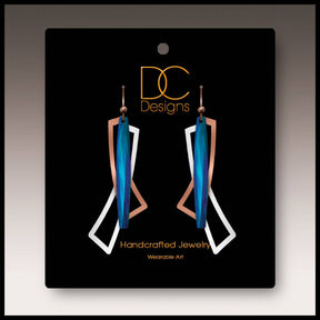 A pair of modern blue, silver, and copper geometric open wings earrings (1.75"), handmade in stainless steel, displayed on a black card labeled “DC Designs Handcrafted Jewelry Wearable Art.”.