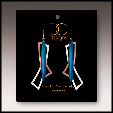 A pair of modern blue, silver, and copper geometric open wings earrings (1.75"), handmade in stainless steel, displayed on a black card labeled “DC Designs Handcrafted Jewelry Wearable Art.”.