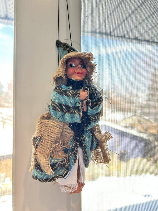 The Kitchen Witch: Philippa Beige Kitchen Witch Doll, featuring a burlap hat and plaid shawl, hangs by a string in front of a sunny window, bringing good luck to your kitchen.