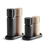 The Shakers Salt and Pepper Grinder Set from Sweden includes four wooden cylindrical pieces, two in sleek black and two in light ash wood, with durable ceramic grinders. These elegant items rest on small trays, blending functionality with minimalist style.