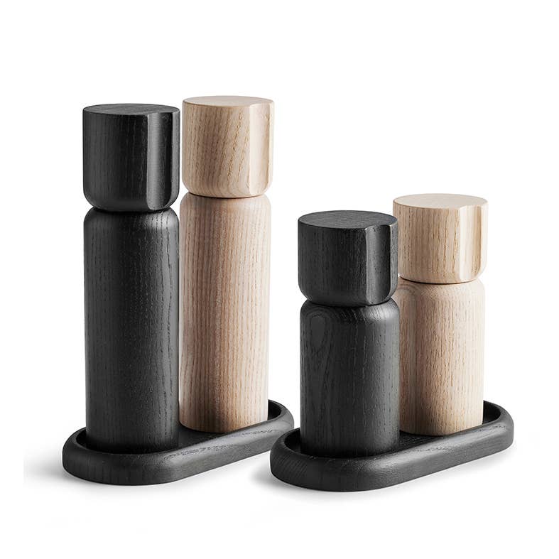 The Shakers Salt and Pepper Grinder Set from Sweden includes four wooden cylindrical pieces, two in sleek black and two in light ash wood, with durable ceramic grinders. These elegant items rest on small trays, blending functionality with minimalist style.