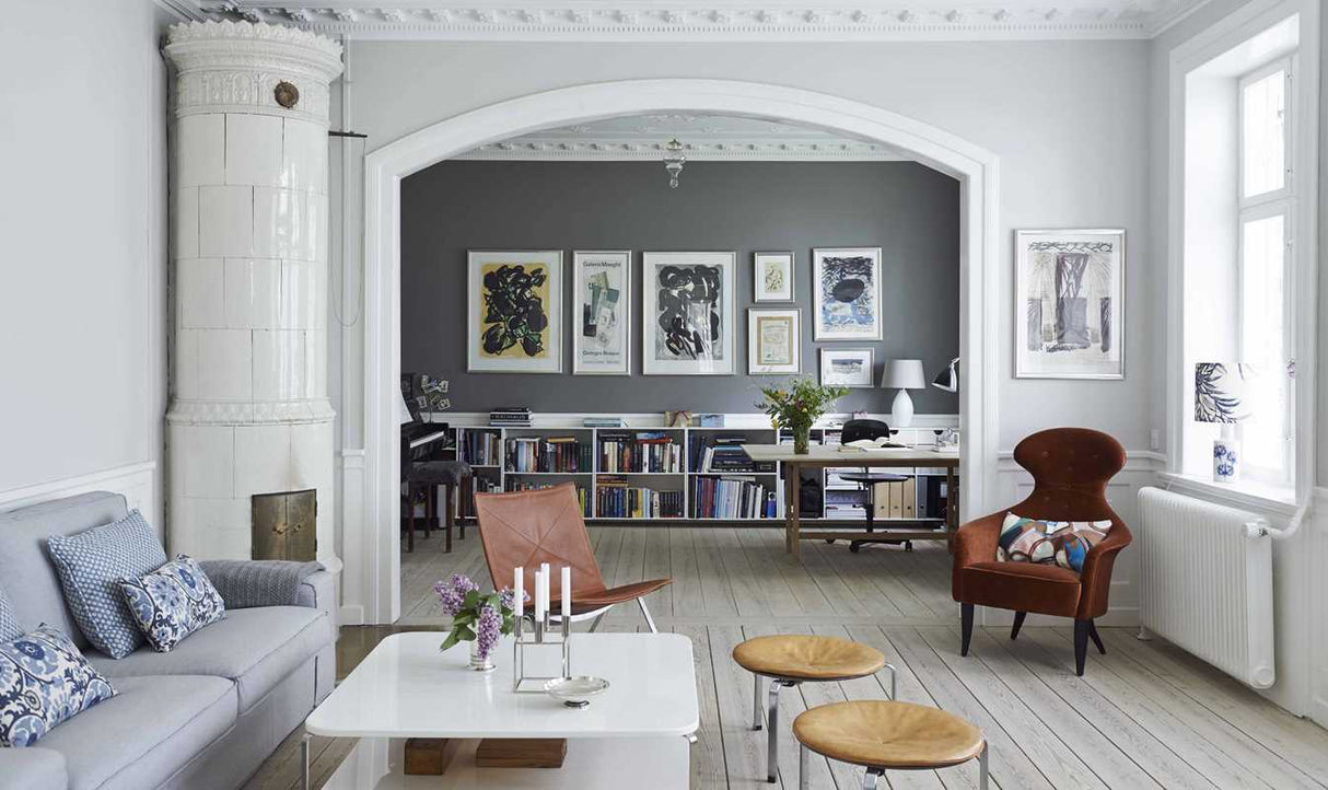 A modern living room with neutral tones and natural light flows into a study area with bookshelves, framed art, and the book Scandinavian Home Interiors Inspired by Light by Niki Brantmark, reflecting timeless Scandinavian style.